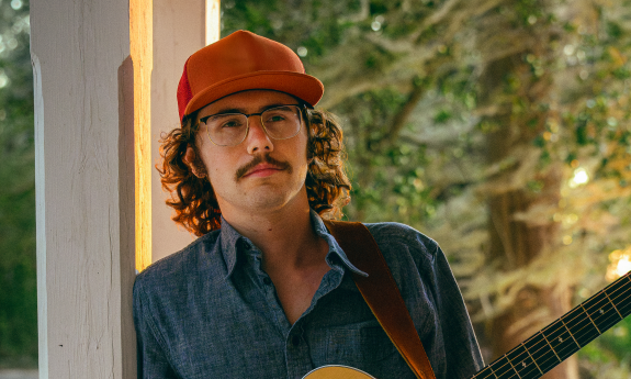 Singer Songwriter Matthew Aiden standing with guitar on a porch.