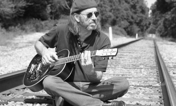 Stava Mala playing his guitar on some train tracks