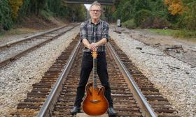 Mark Chirico standing on train tracks with his guitar