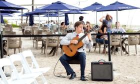 Denis Vasenin playing his guitar at a beach venue.