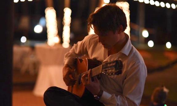 Denis Vasenin playing his guitar at a private event at night.