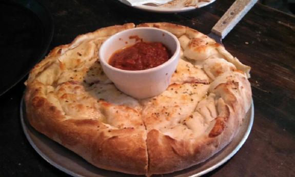 A stuffed meat pizza with a cup of marinara in the middle