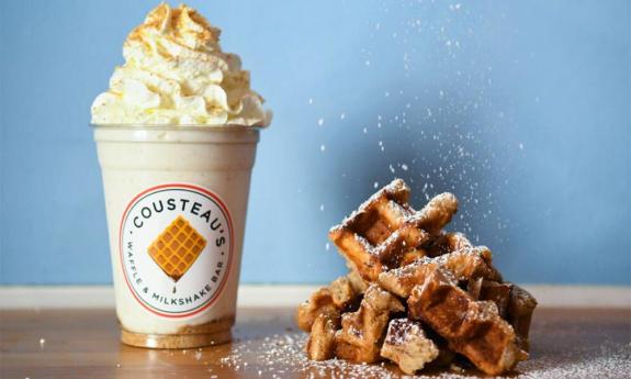 A milkshake topped with whipped cream and a powdered sugar Belgian waffle 