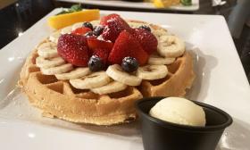 A waffle with fruit on top with a side of butter