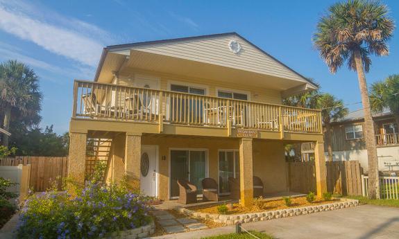 Beneath a blue sky, a welcoming two story Florida beach house with top and ground floor decks populated with outdoor furniture