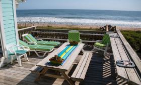  The deck of a vacation blue-painted rental facing the waves of St. Augustine Beach, with green and blue furniture and a long picnic table