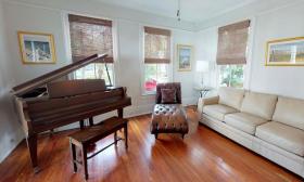A brightly lit sitting room with wood floors, a leather settee and grand piano in a historic vacation rental