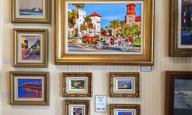 A wall of paintings with scenes from St. Augustine. The Bridge of Lions, the Lightner Museum, and Aviles Street.