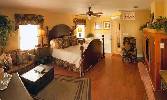 A guest suite at Casa de Solana. A large four poster bed faces a TV set, with a seating area in the foreground. The bathroom is visible through an open door