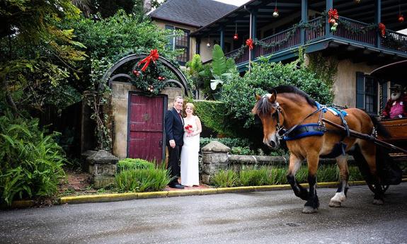 A bride and groom, after their Christmas-season wedding, standing in front of an old gate bedecked with a wreath. Photo by Luna Blu