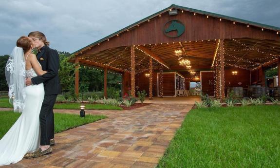 A bride and groom kissing outside of the decorated barn at their Kelly Farm wedding