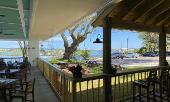 An l-shaped restaurant deck with awning, overlooking a lawn and a view of the river