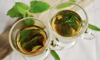 Two cups of herbal tea is positioned on a table. 