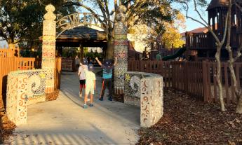 Little kids walking under the entrance sign of the public park