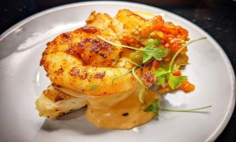 Shrimp with herbs are positioned on a plate. 