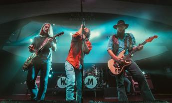 The three frontmen of Whiskey Meyers, performing on stage against a blue light