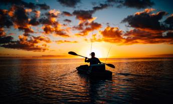 A man steers his kayak and navigates the water during sunset.