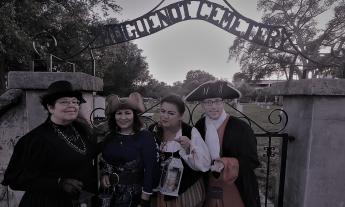 Four ghost tour guides with lanterns standing in front of the cemetary.
