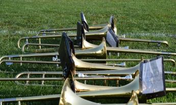 A line of trombones, on the grass in a sports field, with music holders attached