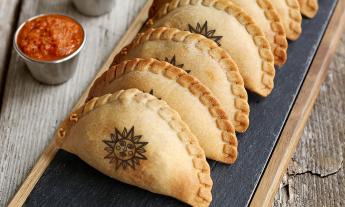 A tray of arranged empanadas with sauce on the side