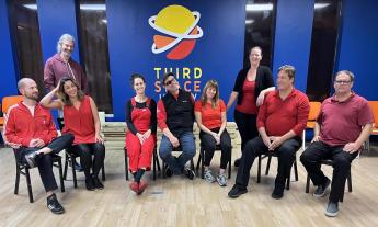 Improv students posing in front of the Third Space Improv logo