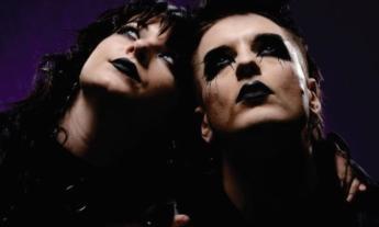 The duo from Vision Video pose with black makeup in front of a dark blue backdrop. 