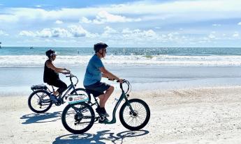 A couple ride bikes from Island Life Bikes on the beach on a sunny day