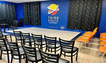 A stage surrounded by orange and black chairs, blue walls, and gold suns and moons on black curtains.