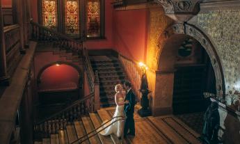 A couple embraces at the marble mosaic entrance to the Ponce Hall Dining Room, backed by Tiffany stained glass windows and warm lighting..