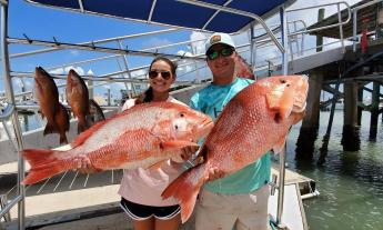 A couple showing off two large red snappers caught during their charter fishing trip with Jodie Lynn Charters