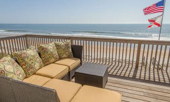 Comfy deck furniture on the balcony of a Ponte Vedra home owned by First Choice FL Vacation Rentals on a sunny beach day. FL and US flags in billow the wind