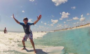 Boy rides a surf board with hands in the air