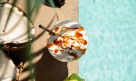 Ellianos cold coffee beverage with caramel and whipped cream on top beside a pool. 