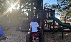 Little boy in a Visit St. Augustine baseball cap walking up Project Swing playground castle stairs. 