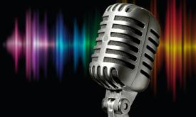 A voice microphone against a black background that is highlighted by multi-colored stage lights
