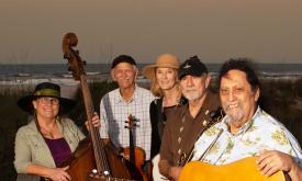 Folk band The Dunehoppers, standing on a sand dune, with their instruments