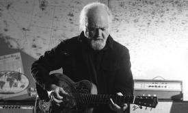 Tinsley Ellis plays his guitar against a backdrop featuring a world map.