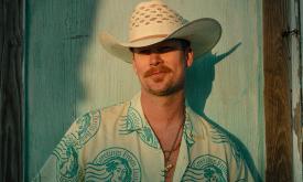 Brian Kelley poses in a white cowboy hat in front of a light blue backdrop.