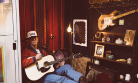 Hudson Westbrook sits in a chair and poses with his guitar.