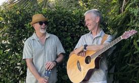 The duo Little Silver standing with guitars in front of hedge, both smiling