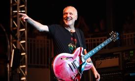 Peter Frampton laughs and points at his audience while performing on stage.