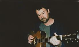 Jordan Tice with his guitar on a dark stage