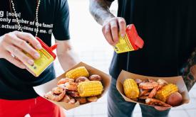 Two men adding seasoning to their shrip boil