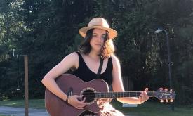Songwriter Alivia Hunter, in a hat, with her guitar, outsite