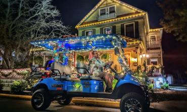 A blue Panda Tours golf cart, decorated with holiday lights, in front of a brightly lit home