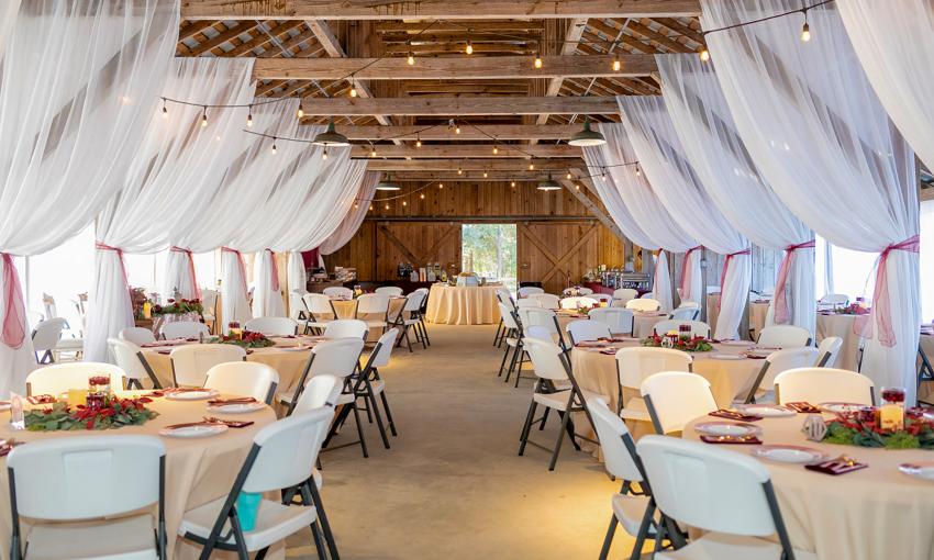 The interior of the barn venue space at Florida Agricultural Museum, decorated for a wedding with draped fabric and round tables