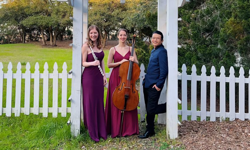 Three members of Astralis Chamber Ensemble, standing under a white gate and pergola in a garden