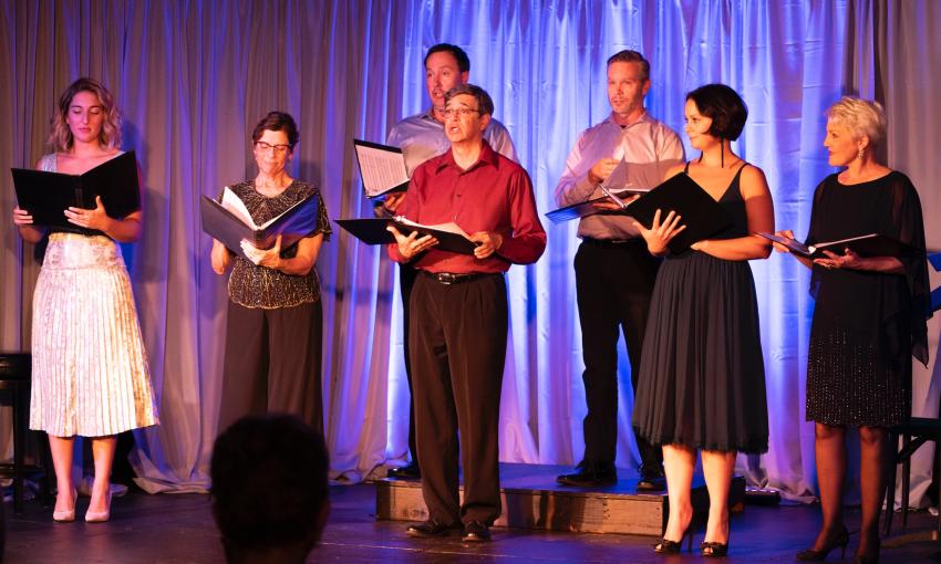 A group of singers on stage with music folders, performing