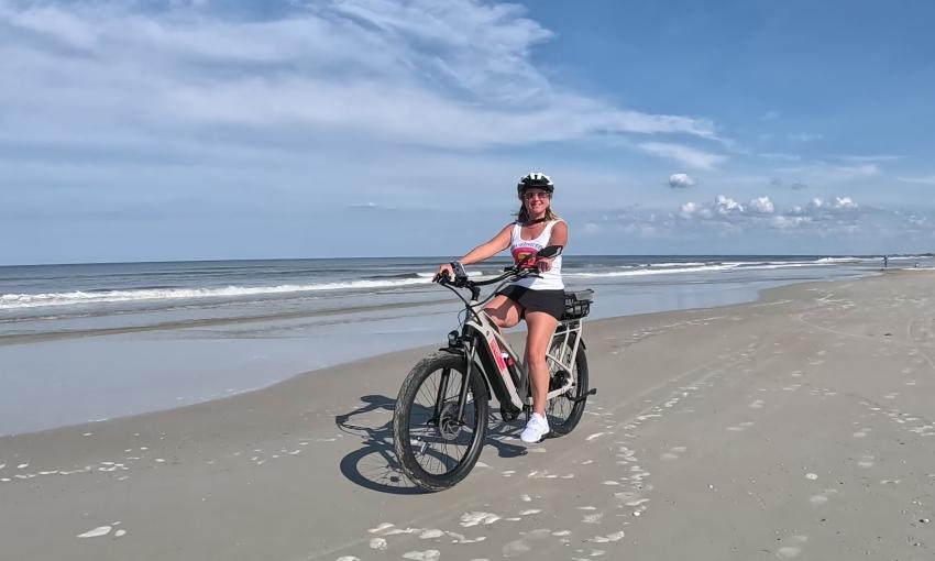 A woman biking on the beach with a bike from Sun and Fun E-Bike Rentals