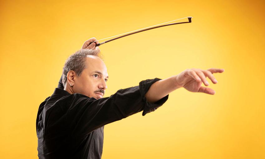 Violinst Luca Ciarla gesturing with his bow, on stage in front of a yellow background